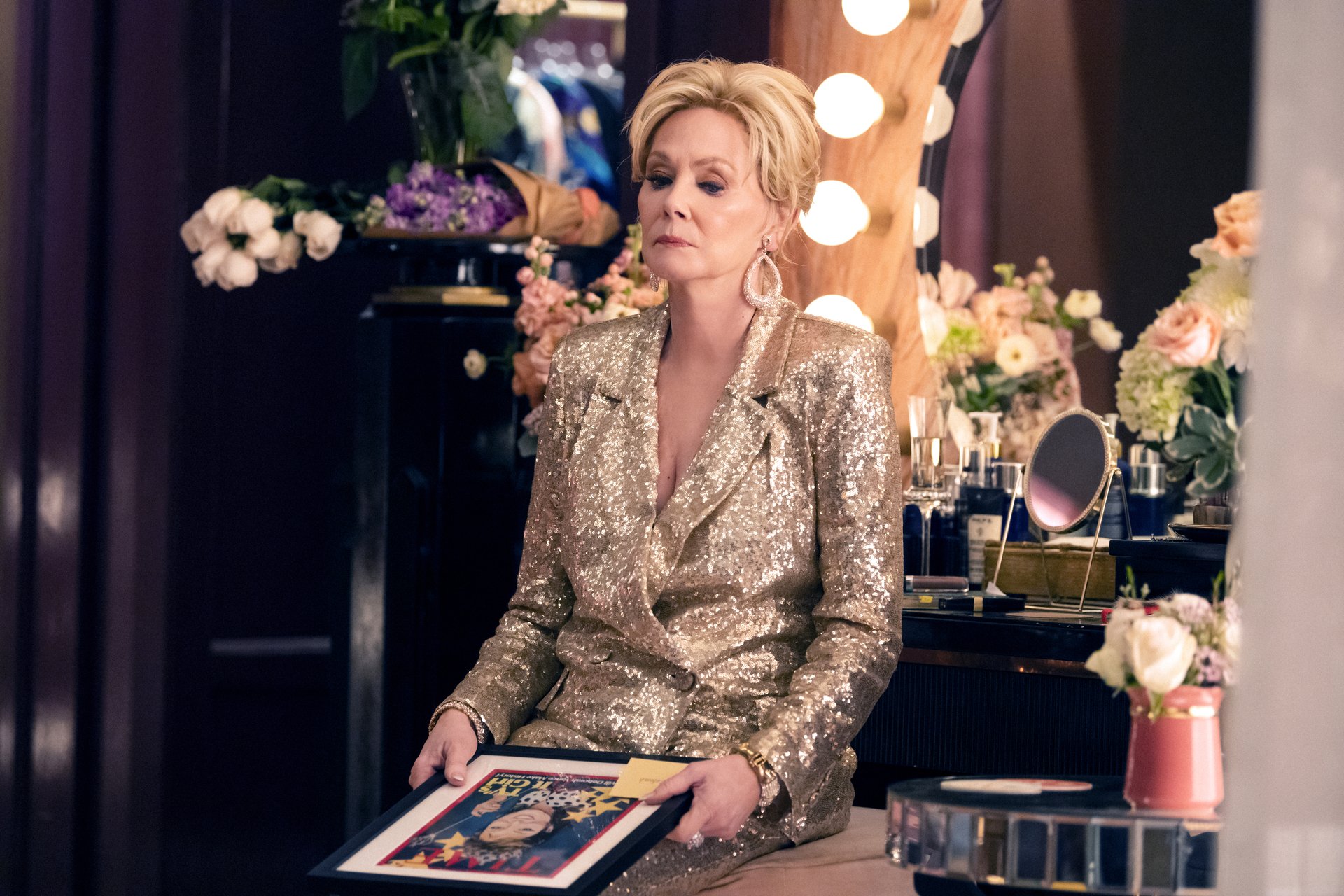 HD desktop wallpaper featuring a scene from the TV show Hacks (2021), depicting a woman in a gold suit seated backstage surrounded by flowers and makeup.