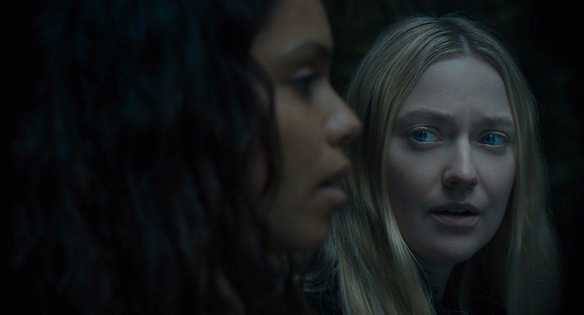 HD desktop wallpaper featuring a scene from the movie The Watchers (2024) with Dakota Fanning. The image showcases a close-up interaction between two characters in a dark and intense setting.