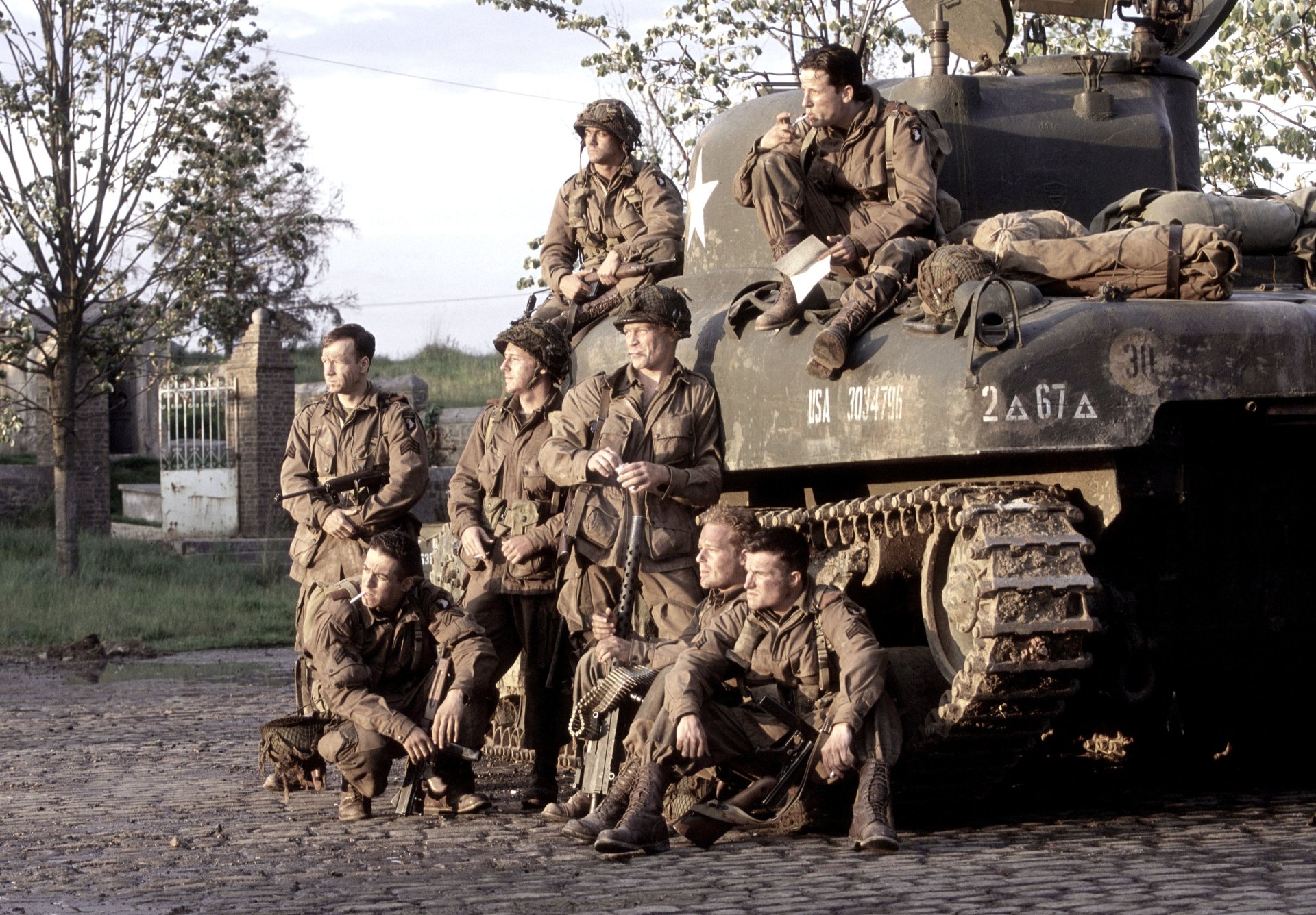 A HD desktop wallpaper from the TV show Band of Brothers, depicting soldiers in WWII uniforms posing around a tank.
