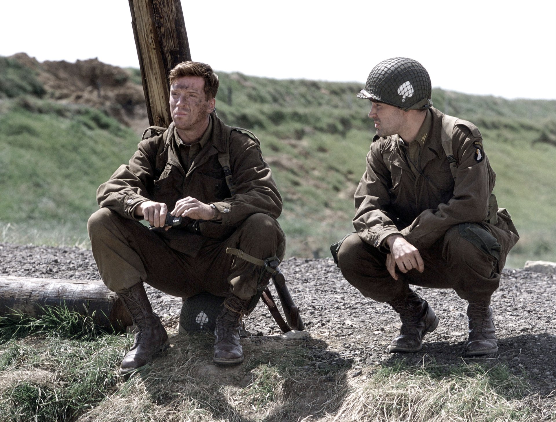 Two soldiers from the TV show Band of Brothers sit and crouch on a grassy field in this HD desktop wallpaper and background.