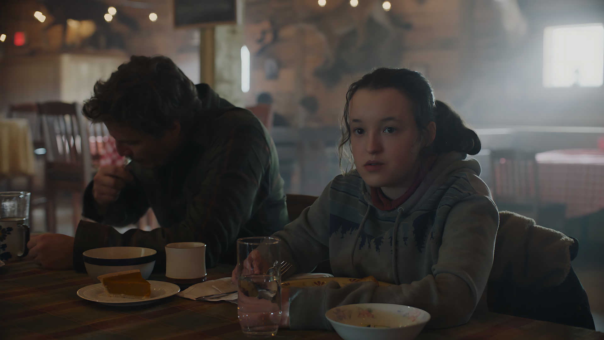 Two weary survivors at a dim diner table with bowls and mugs, moody scene from The Last Of Us — 8K Ultra HD PC desktop wallpaper and background.
