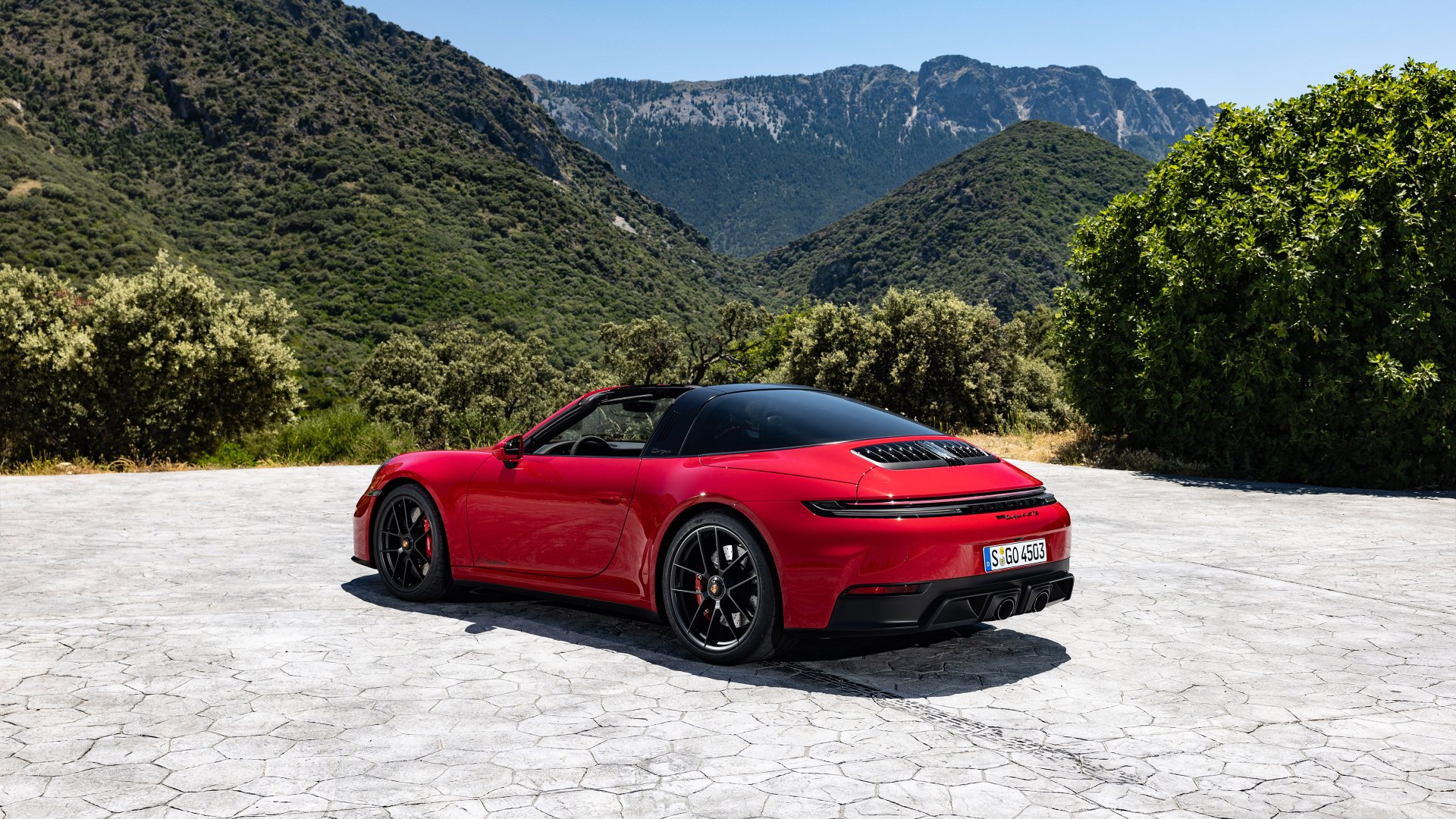 A stunning HD desktop wallpaper featuring a red Porsche 911 Targa 4 GTS parked on a scenic mountain background with lush greenery.