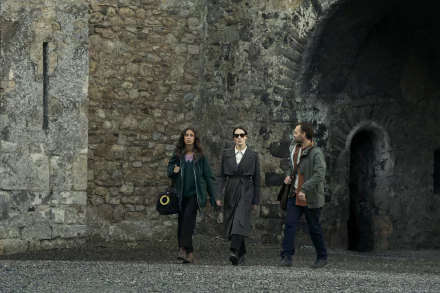 HD wallpaper from the TV show Bodkin featuring three characters walking confidently in front of an ancient stone wall.