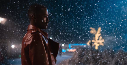 HD desktop wallpaper of Ncuti Gatwa from the 2023 Doctor Who TV show, featuring him in a red jacket with snow falling at night.