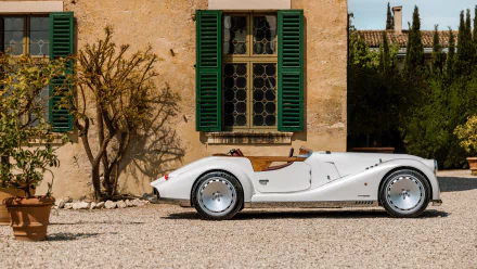 HD desktop wallpaper of a classic white Morgan Midsummer car parked in front of a rustic building with green shutters, set against a serene outdoor background.