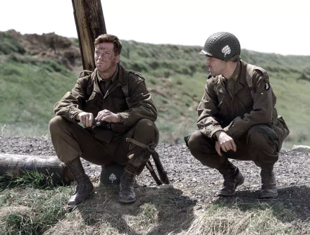 Two soldiers from the TV show Band of Brothers sit and crouch on a grassy field in this HD desktop wallpaper and background.