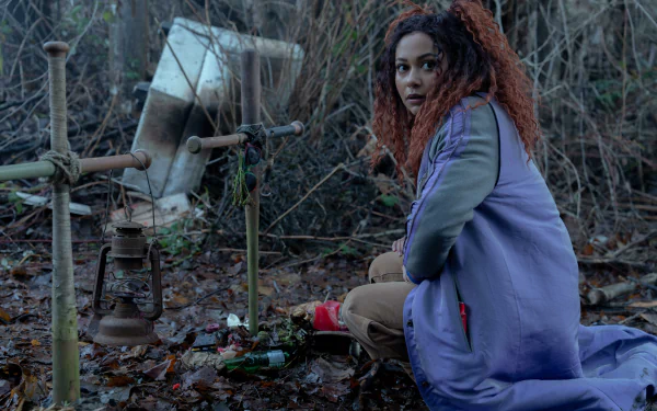 HD desktop wallpaper from the TV show Dead Boy Detectives featuring a woman sitting in a wooded area with a thoughtful expression.