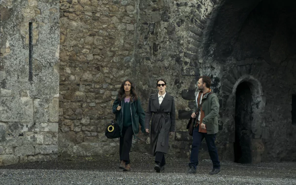 HD wallpaper from the TV show Bodkin featuring three characters walking confidently in front of an ancient stone wall.