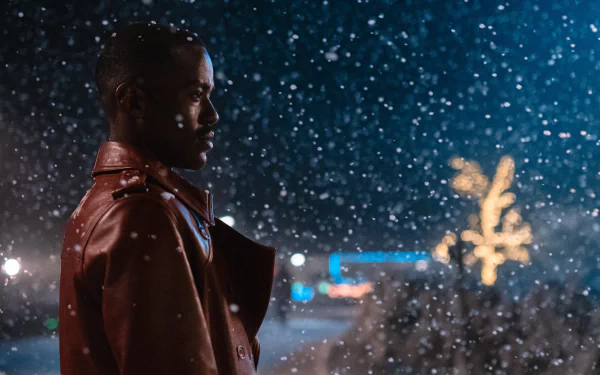 HD desktop wallpaper of Ncuti Gatwa from the 2023 Doctor Who TV show, featuring him in a red jacket with snow falling at night.