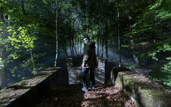 A haunting scene from The Strangers: Chapter 1 movie in HD resolution, set in a misty, dark forest, featuring a masked character standing on a pathway, making for a chilling desktop wallpaper and background.