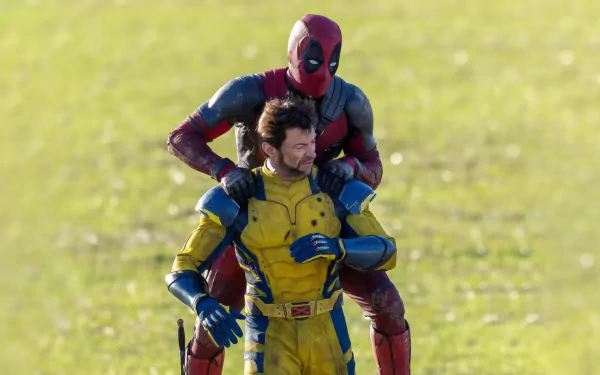HD wallpaper featuring Deadpool and Wolverine from the movie, showing Deadpool standing behind Wolverine outdoors on a sunny day.
