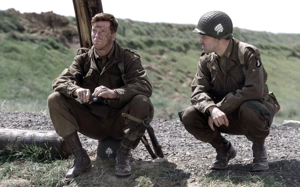 Two soldiers from the TV show Band of Brothers sit and crouch on a grassy field in this HD desktop wallpaper and background.