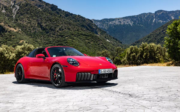 A red Porsche 911 Targa 4 GTS parked on a scenic mountain road, captured as a high-definition desktop wallpaper and background. The car stands out vividly against the lush green hills and blue sky.