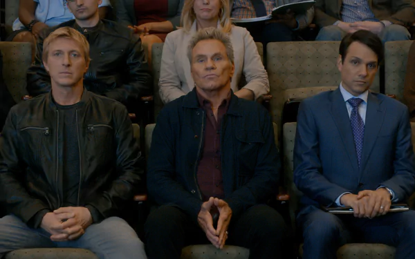 HD desktop wallpaper featuring characters from the TV show Cobra Kai seated in an auditorium, portraying a tense moment.