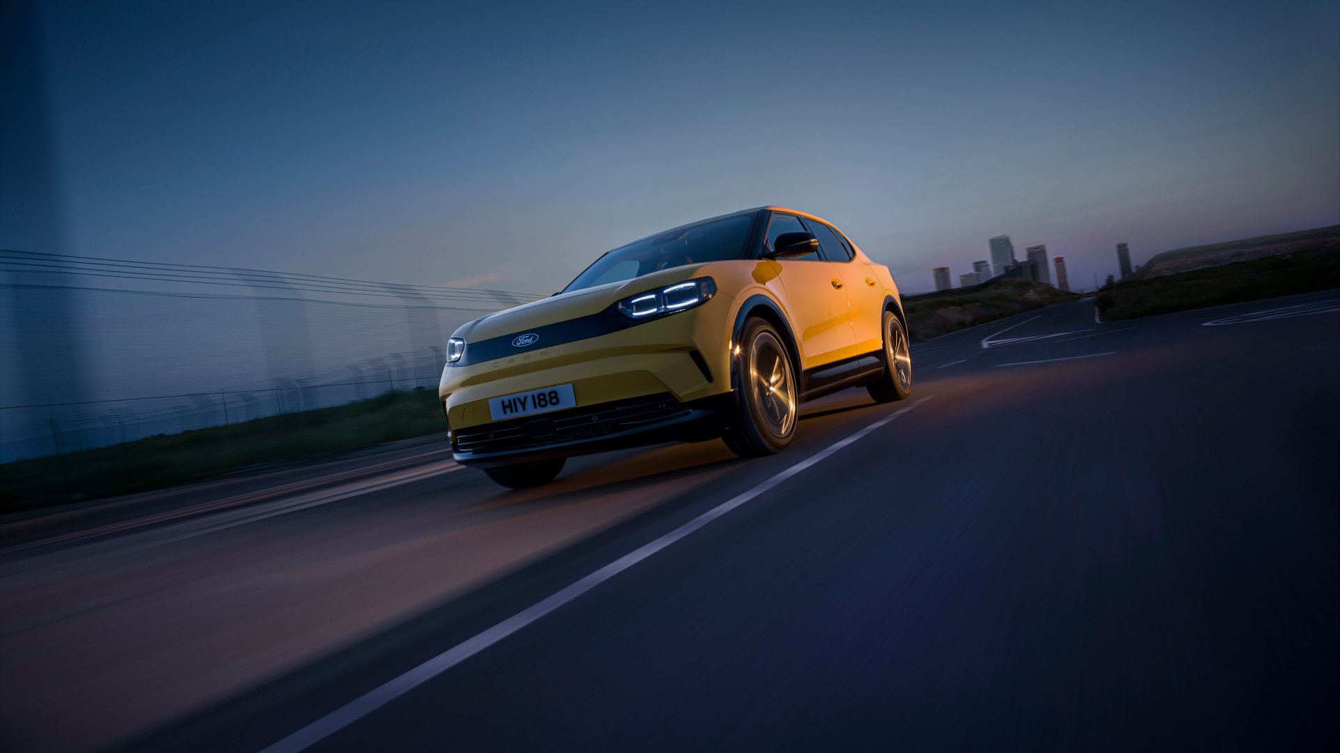 A striking HD wallpaper featuring a dynamic Ford Capri in vibrant yellow, captured on a road at dusk, highlighting its sleek design and modern appeal.