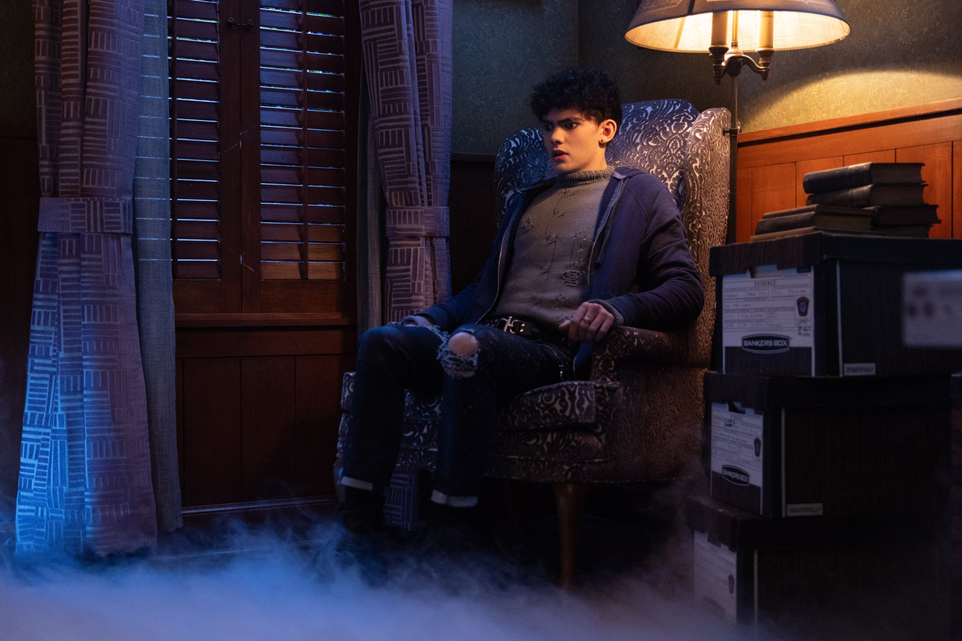A moody HD desktop wallpaper featuring a character sitting in a vintage armchair, surrounded by fog and shadows, capturing the eerie vibe of Agatha All Along.