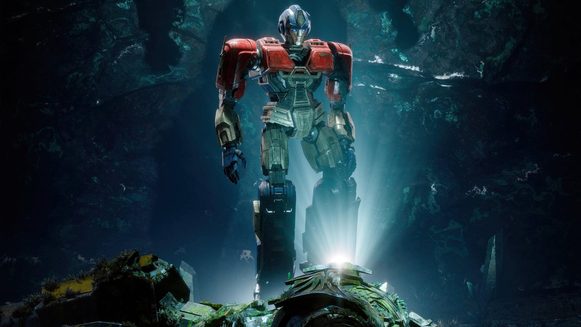 Transformers One 2K Quad HD PC desktop wallpaper — a towering red-and-blue Autobot stands illuminated in a dark, ruined cavern above smashed machinery.