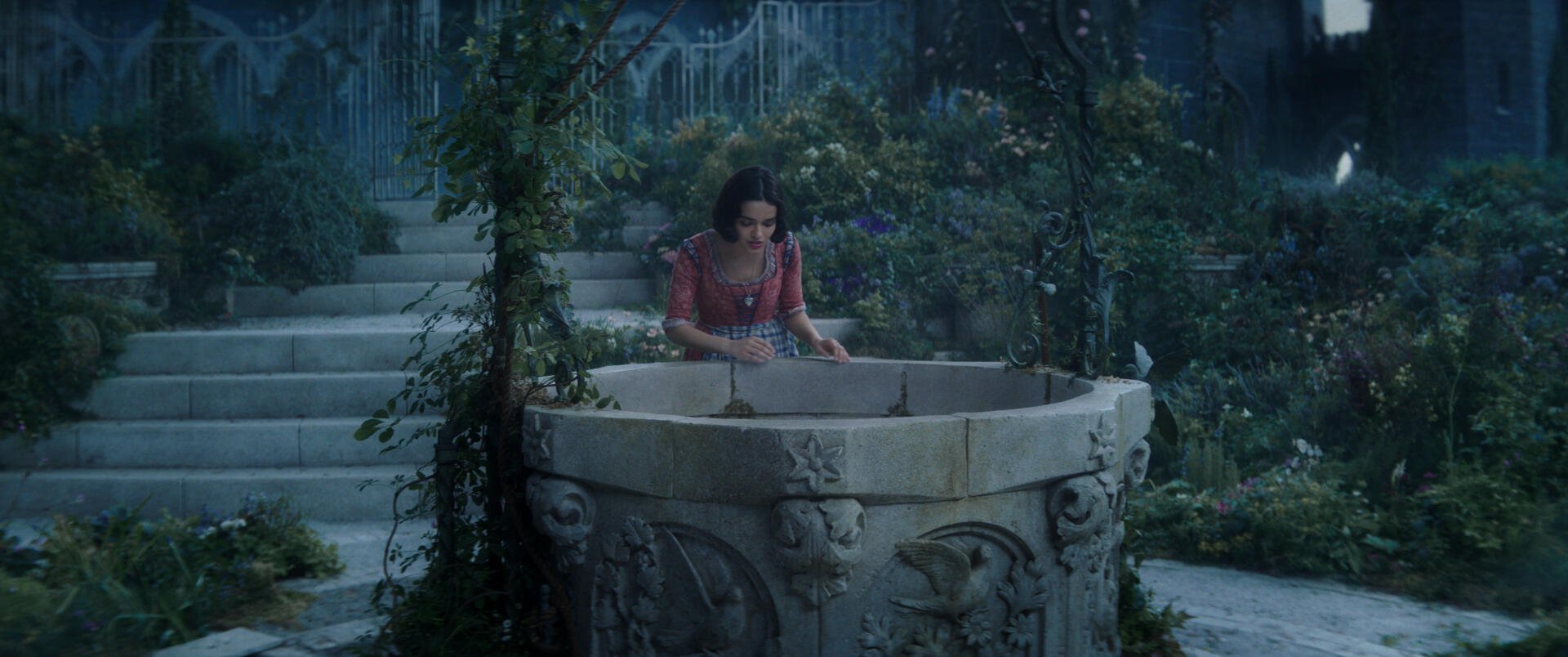 A scene from the movie Snow White (2025) featuring Snow White by a beautifully detailed stone well, surrounded by lush greenery and a serene, enchanting atmosphere.