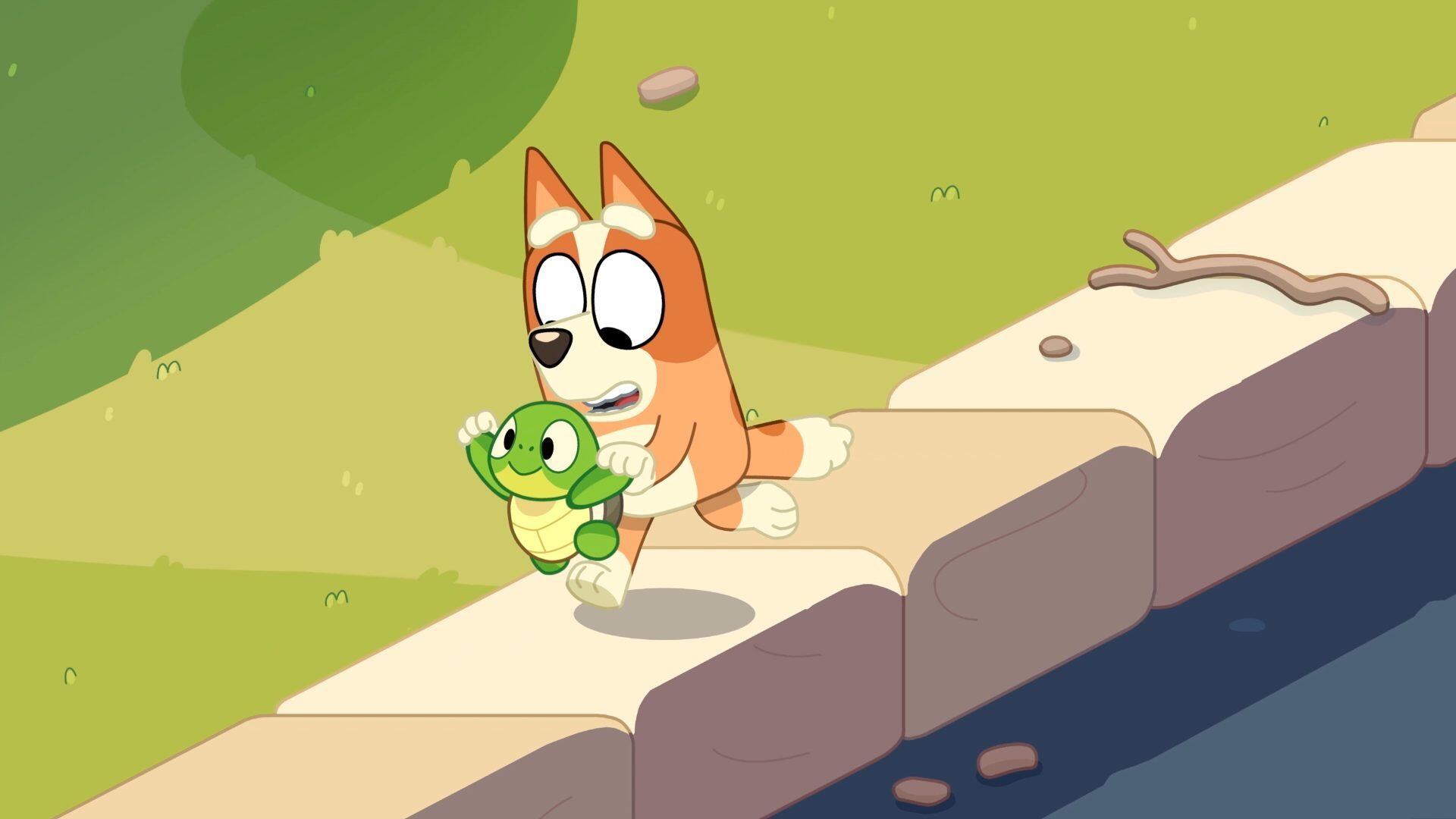 A vibrant HD wallpaper featuring Bluey, the playful puppy, joyfully carrying a green turtle toy along a riverbank, surrounded by lush greenery.