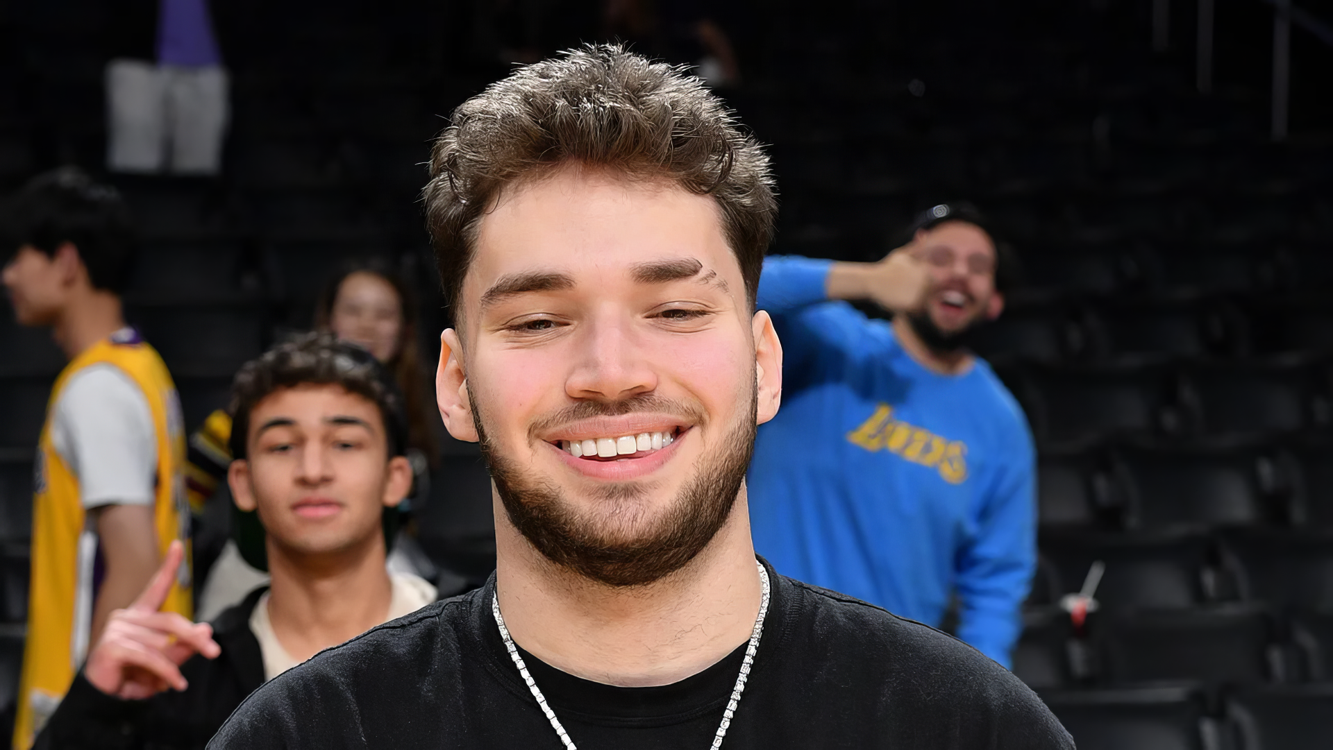 A high-definition desktop wallpaper featuring streamer Adin Ross, smiling in a lively setting with fans in the background, capturing a moment of joy and energy.