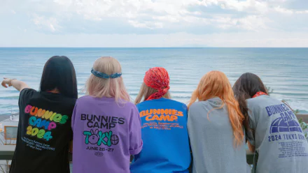 A vibrant HD wallpaper featuring five friends in colorful sweatshirts, enjoying the ocean view, capturing a carefree moment tied to NewJeans music culture.