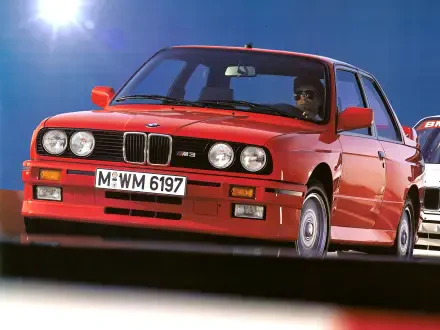 A vibrant red BMW E30 M3 drives forward, showcasing its classic design. This high-definition image serves as a striking PC desktop wallpaper and background.