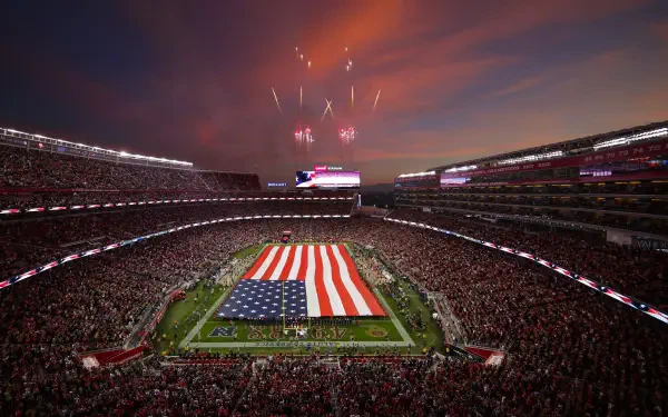 A vibrant San Francisco 49ers football game scene, showcasing a packed stadium under a stunning sunset, with an oversized American flag on the field and fireworks lighting the sky.
