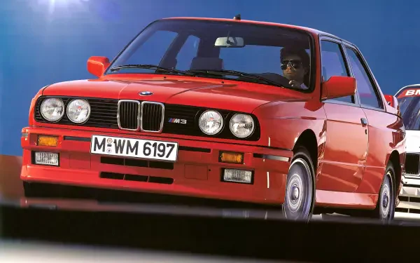 A vibrant red BMW E30 M3 drives forward, showcasing its classic design. This high-definition image serves as a striking PC desktop wallpaper and background.