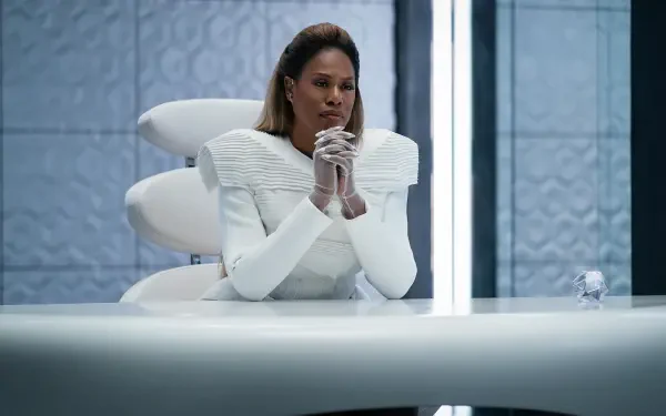 A still from the movie Uglies, featuring Laverne Cox in a futuristic setting, seated at a sleek white table with a thoughtful expression. 4K Ultra HD wallpaper background.