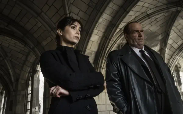 A dramatic scene from the TV show The Penguin featuring Cristin Milioti and Colin Farrell, set against a gothic architectural backdrop, showcasing intense expressions and strong characters.