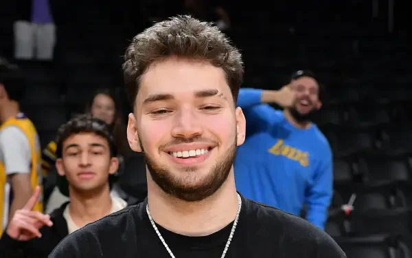A high-definition desktop wallpaper featuring streamer Adin Ross, smiling in a lively setting with fans in the background, capturing a moment of joy and energy.