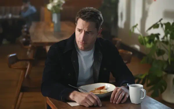 Justin Hartley appears contemplative at a dining table in a scene from the TV show Tracker (2024), featuring a warm, inviting background with plants and soft lighting.