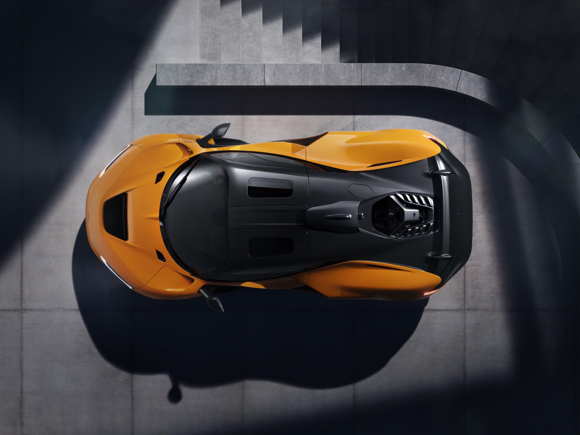 An overhead view of a McLaren W1, showcasing its sleek design and vibrant orange color against a modern architectural backdrop. This 8K Ultra HD image serves as a striking desktop wallpaper.