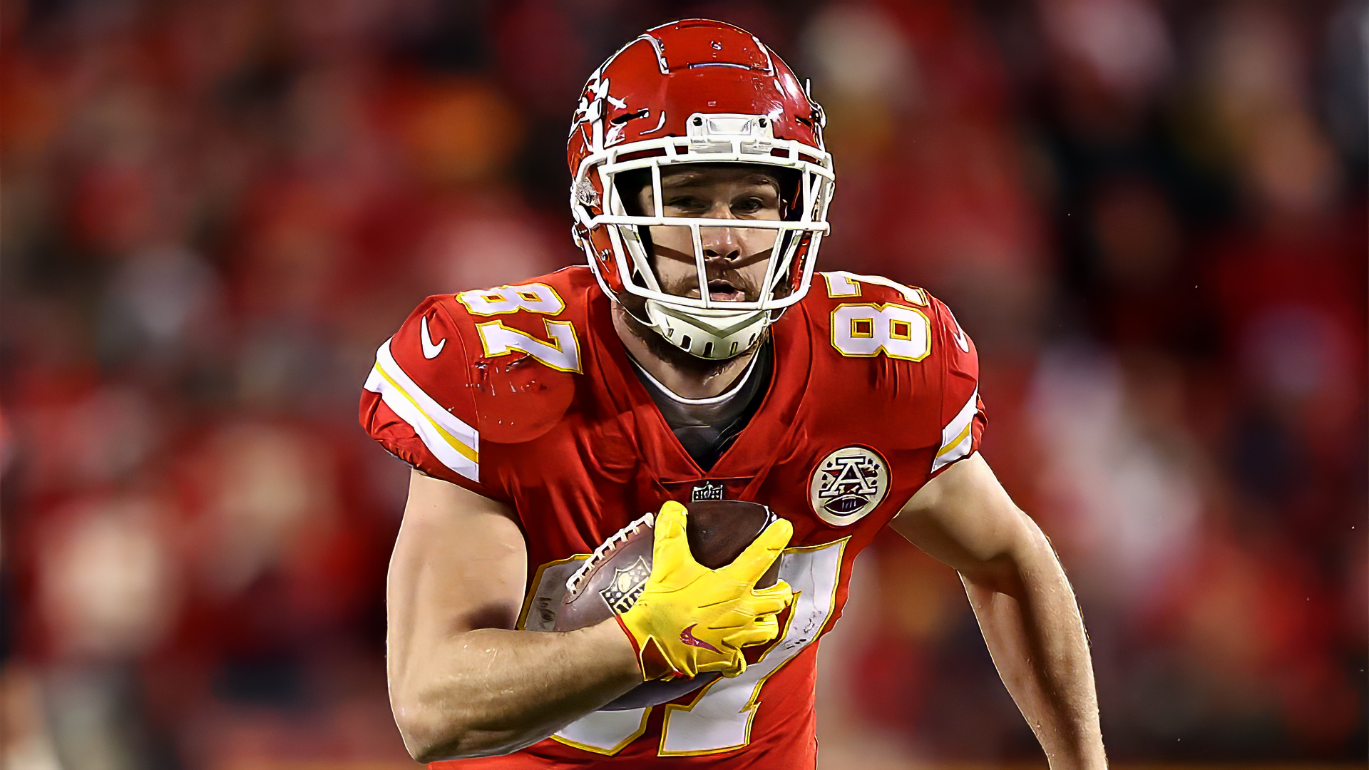 Travis Kelce of the Kansas City Chiefs runs with the football during an NFL game, captured in this dynamic HD desktop wallpaper featuring vibrant team colors.