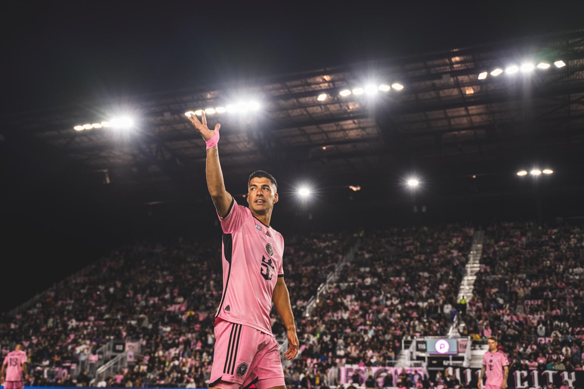 Luis Suárez gestures to fans while playing for Inter Miami CF, illuminated by bright stadium lights in a vibrant atmosphere, captured in stunning 4K Ultra HD detail.