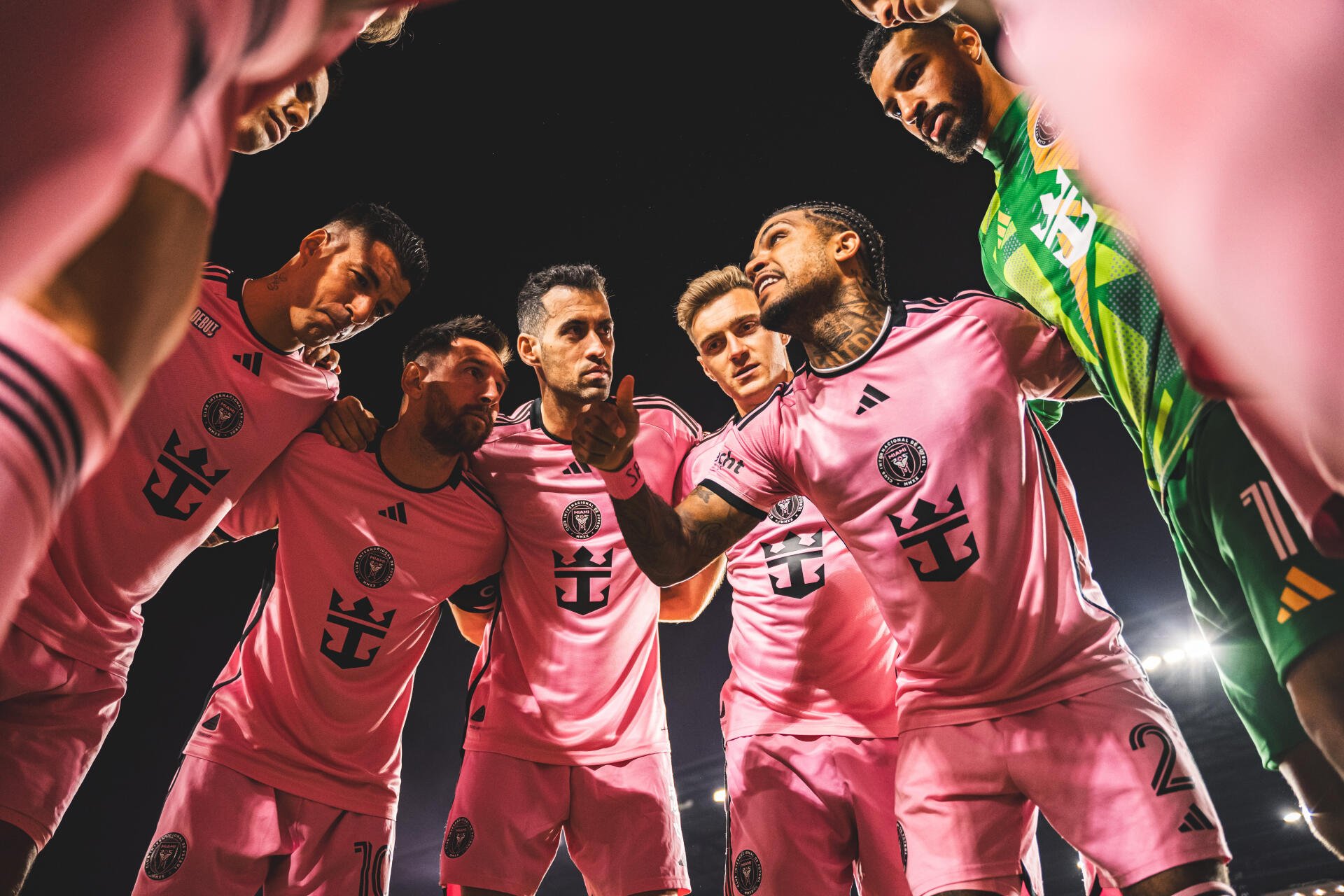 A vibrant 4K Ultra HD image of Inter Miami CF players, including Luis Suárez, Lionel Messi, and Sergio Busquets, huddled together in their iconic pink jerseys.