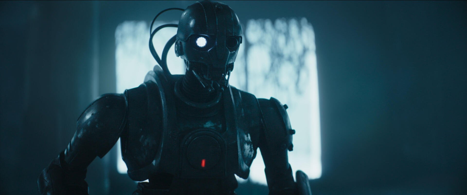 A detailed HD wallpaper from the TV show Star Wars: Skeleton Crew, featuring a futuristic robot with glowing eyes against a dimly lit backdrop.