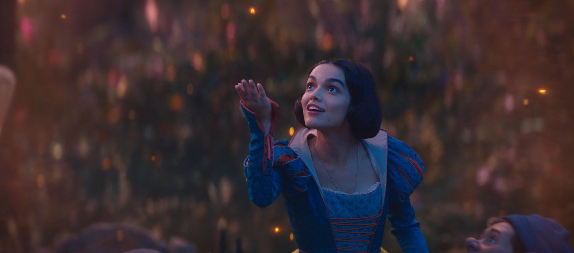 Rachel Zegler as Snow White in a vibrant scene from the 2025 movie. The image captures her expression of wonder against a magical background filled with soft lights.