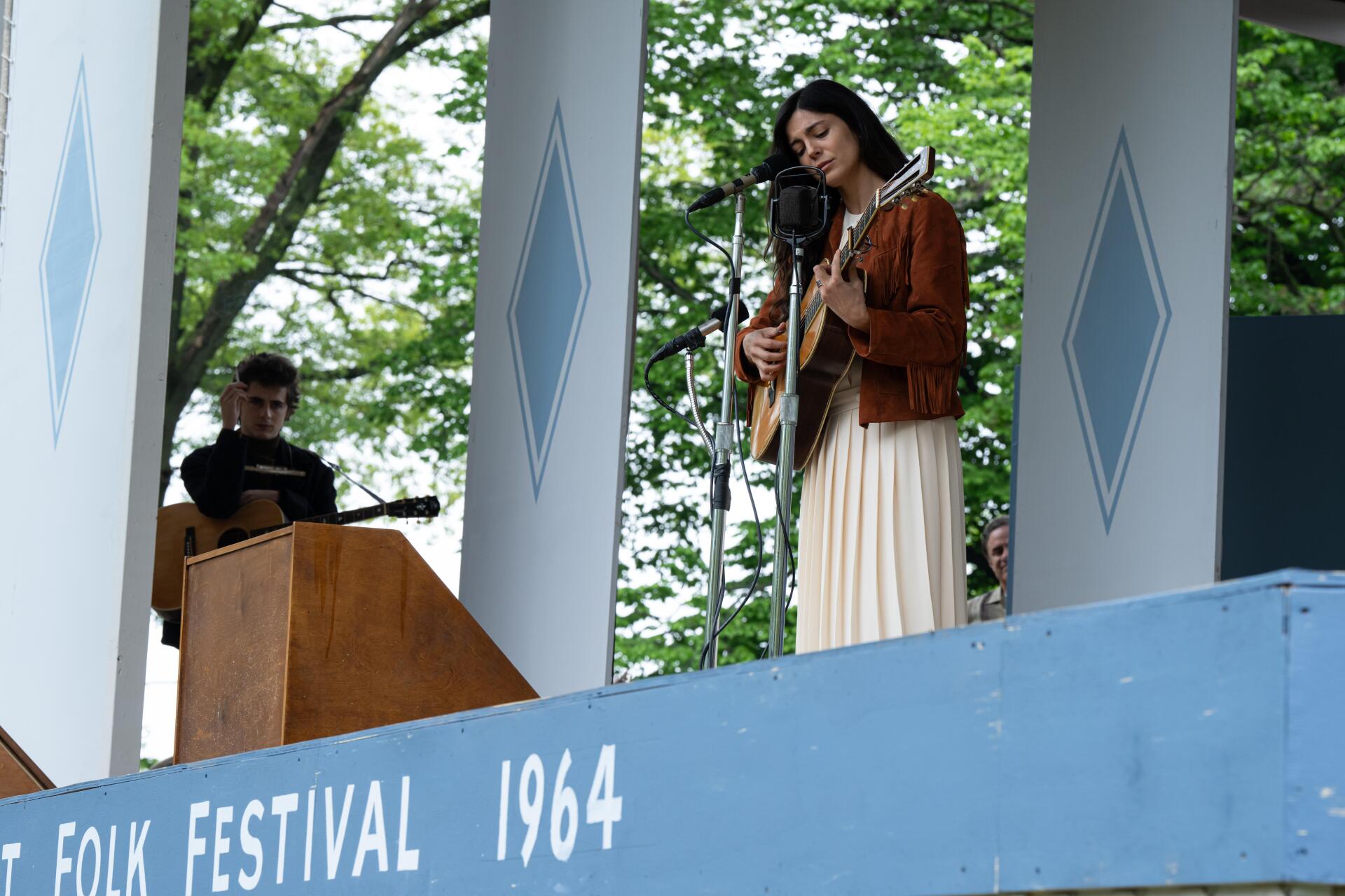 A woman performs as a singer on stage at a 1964 folk festival, featured in the movie A Complete Unknown, showcasing Monica Barbaro in an 8K Ultra HD scene.