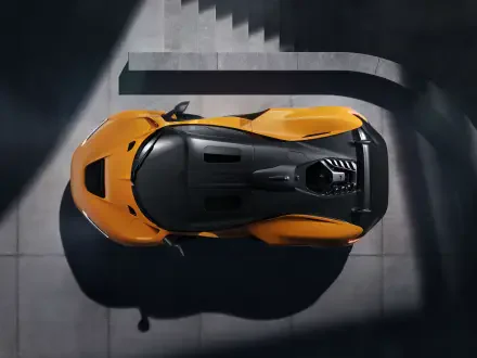 An overhead view of a McLaren W1, showcasing its sleek design and vibrant orange color against a modern architectural backdrop. This 8K Ultra HD image serves as a striking desktop wallpaper.