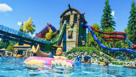 A vibrant scene from Planet Coaster 2, showcasing a water park with colorful slides and a kid enjoying a float in a sparkling blue pool under a clear sky.