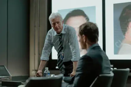 A scene from the TV show The Agency featuring Richard Gere, showcasing a tense discussion in a modern meeting room with images projected on a screen.
