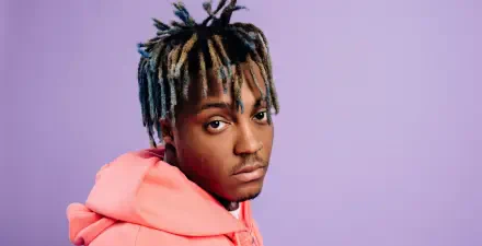 Juice Wrld poses against a purple backdrop, showcasing his distinct hairstyle and style. This HD image serves as a vibrant desktop wallpaper for music enthusiasts.