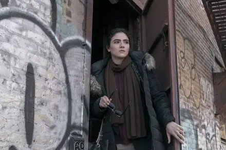 A scene from the TV show The Night Agent, featuring Arienne Mandi standing in a doorway, holding glasses, against a backdrop of graffiti, captured in an HD wallpaper format.
