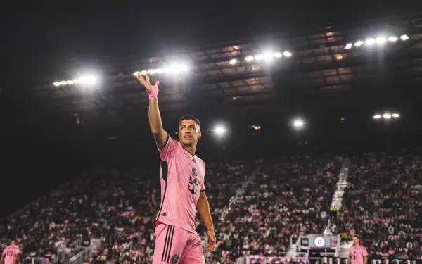 Luis Suárez gestures to fans while playing for Inter Miami CF, illuminated by bright stadium lights in a vibrant atmosphere, captured in stunning 4K Ultra HD detail.