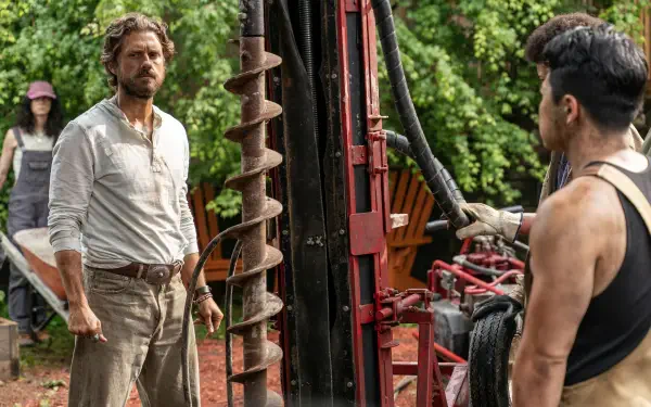 A scene from the TV show Earth Abides, featuring two men at a drilling site surrounded by lush greenery, capturing a moment of tension and collaboration. HD desktop wallpaper.