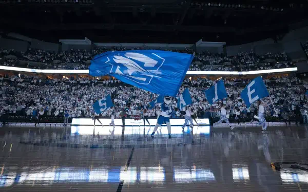 A dynamic Creighton Bluejays scene featuring enthusiastic fans in a packed arena, with cheerleaders waving blue flags, creating an energetic atmosphere for basketball.