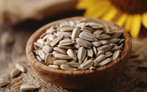 A close-up of a wooden bowl filled with sunflower seeds, set against a backdrop of natural textures, accompanied by a sunflower, captured in 4K Ultra HD quality.