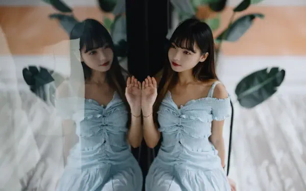 Woman in a pale blue dress touching a glass reflection against a soft leafy backdrop — 8K Ultra HD PC desktop wallpaper.