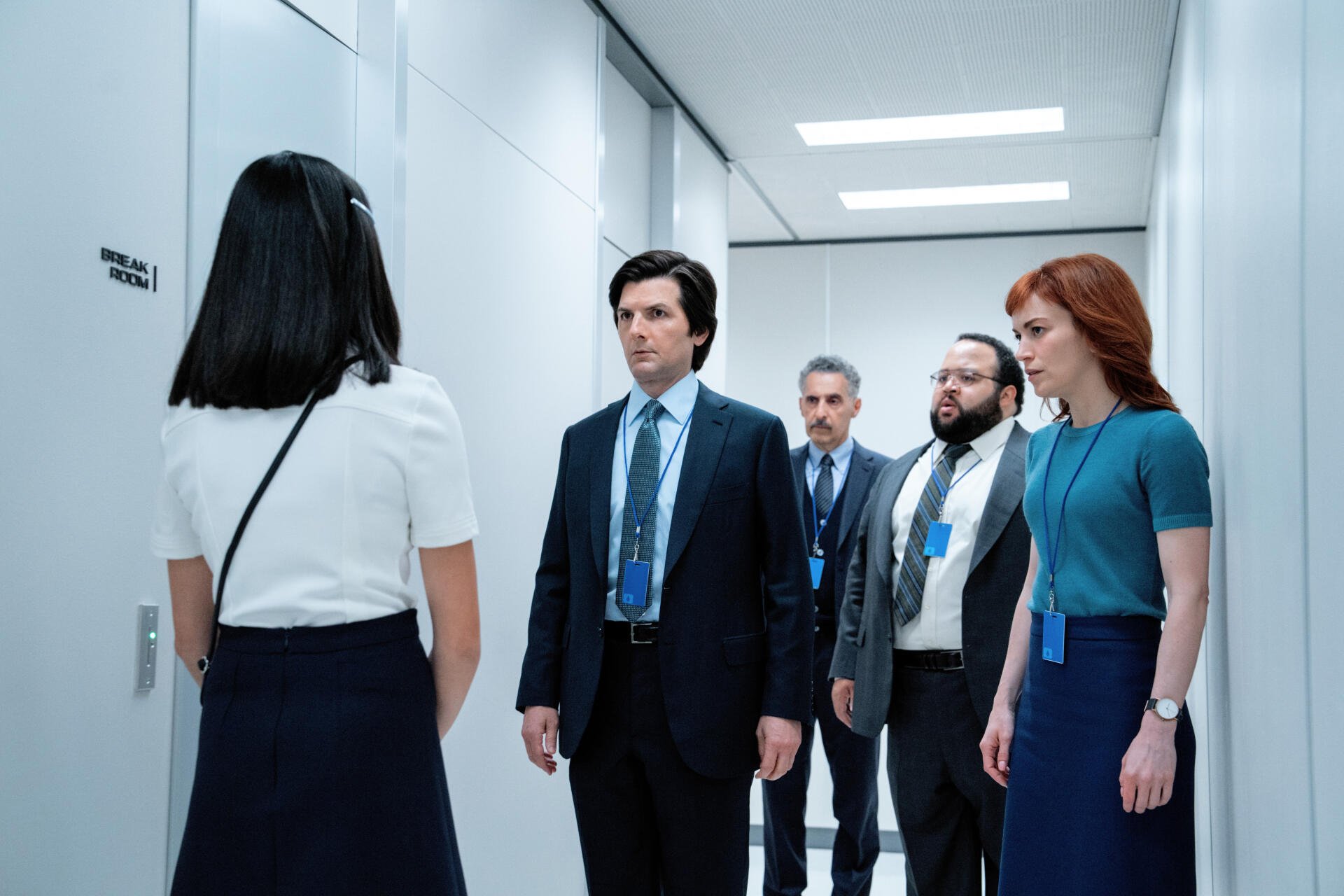 A scene from the TV show Severance featuring John Turturro, Adam Scott, and Britt Lower, walking through a stark corridor in a corporate setting. High-resolution 4K Ultra HD.